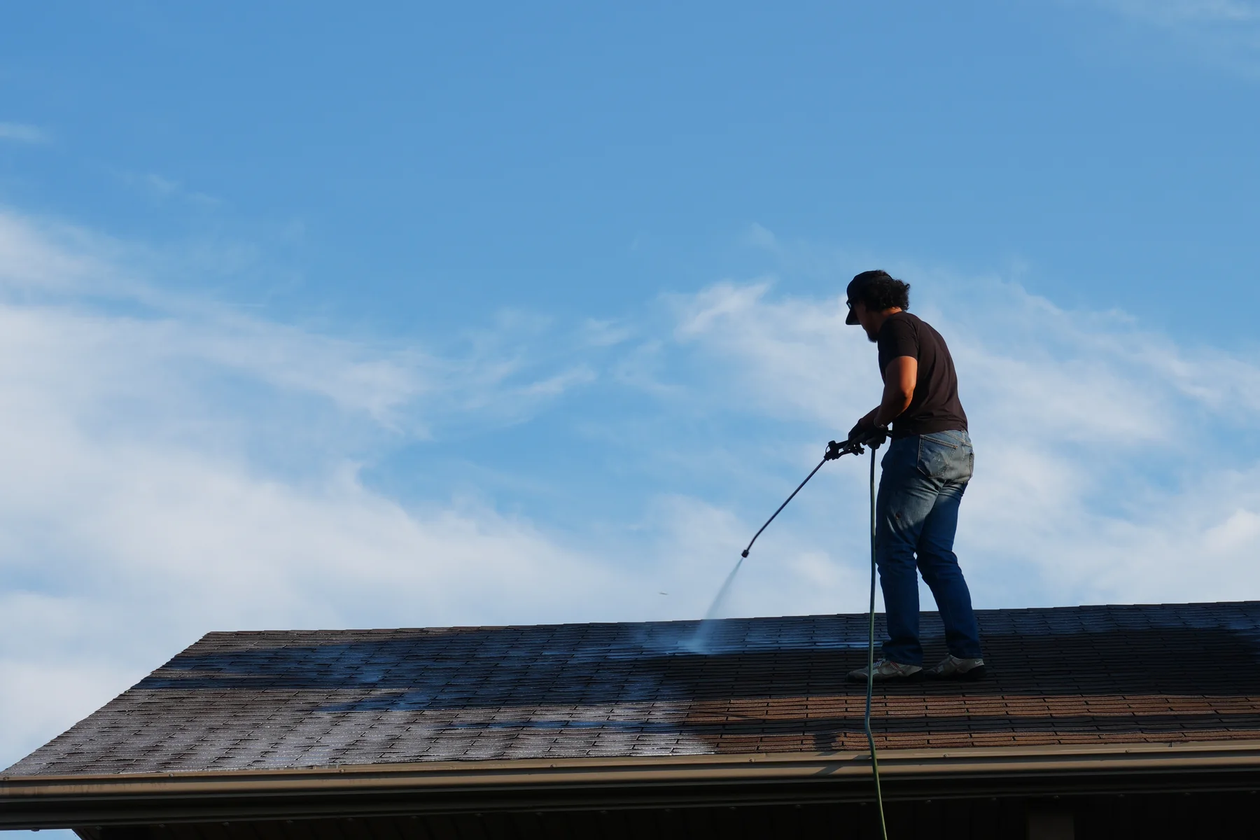 Revive Your Roof technician spraying rejuvenation treatment across an asphalt shingle roof