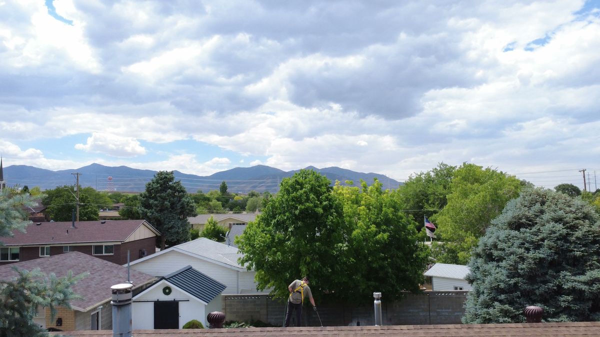 Drone view across a Wasatch Front neighborhood with the mountains behind and a Revive Your Roof technician working on a roof in the foreground